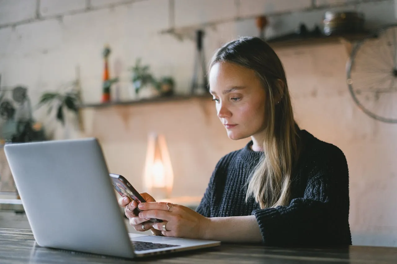 Woman using a smartphone and laptop to gather files and assets for a website project.