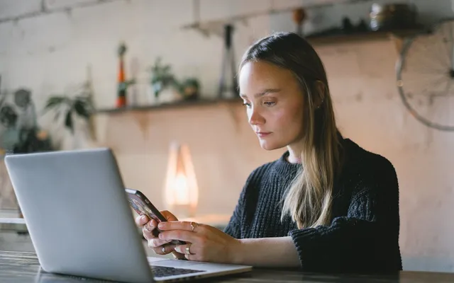 Woman using a smartphone and laptop to gather files and assets for a website project.