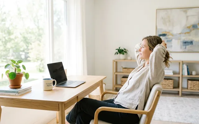 A woman leaning back in her desk chair with her hands locked behind her head, relaxed at the end of a completed workday